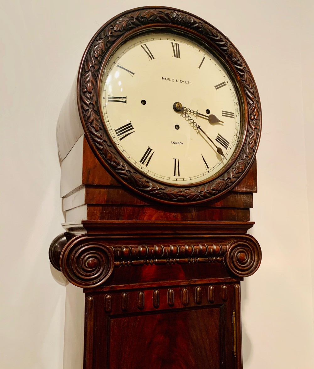 An Edwardian dark mahogany longcase clock featuring a circular white dial with Roman numerals, carved ionic capital columns, and a panelled base. View III