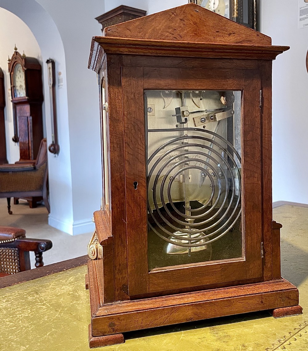 A Victorian pollard oak bracket clock featuring an engraved white dial, Roman numerals, and gilt scrollwork accents. View V