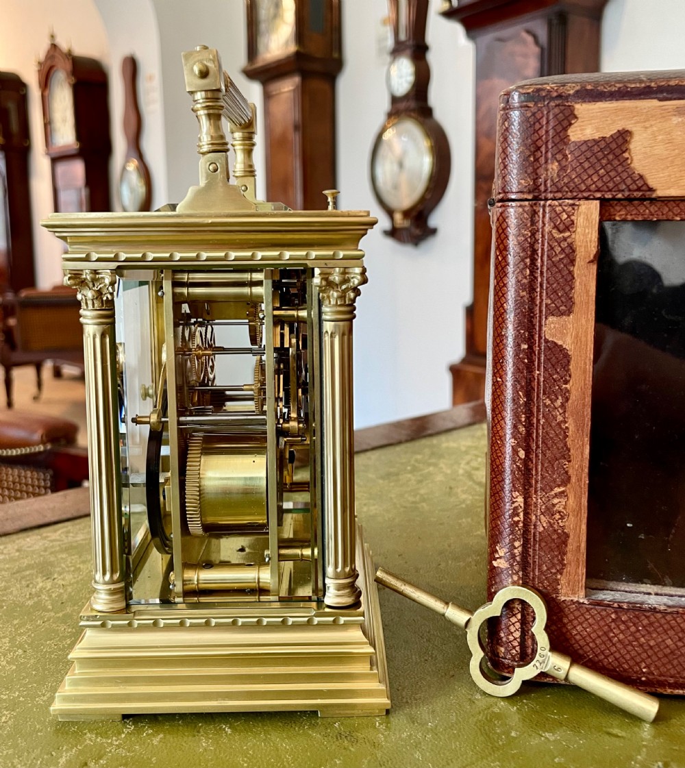 An antique brass French carriage clock with fluted corner columns, Corinthian capitals, a white enamel dial with Roman numerals, and a top handle. View II