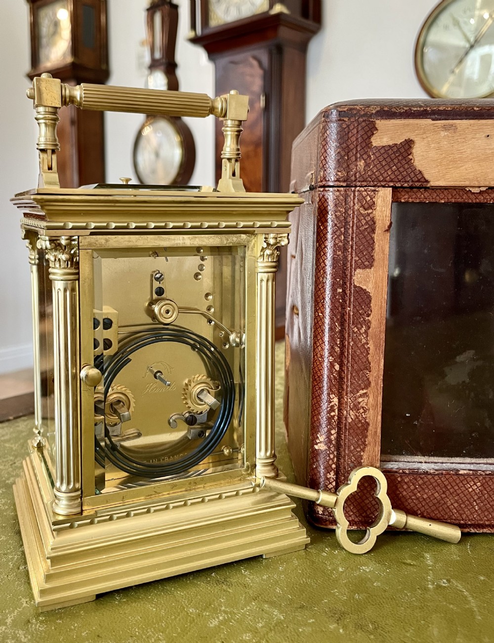 An antique brass French carriage clock with fluted corner columns, Corinthian capitals, a white enamel dial with Roman numerals, and a top handle. View IV