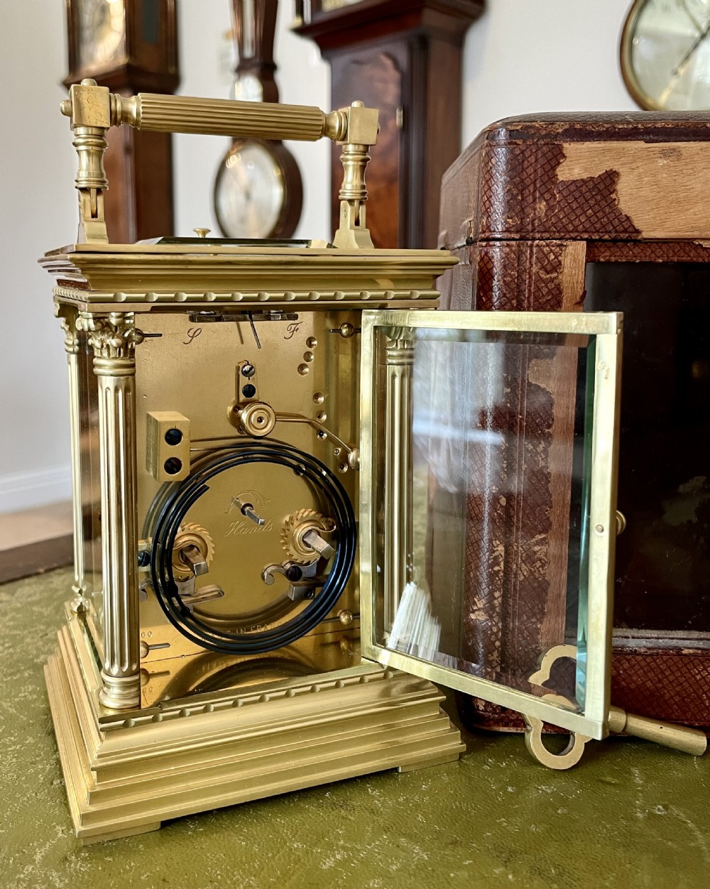 An antique brass French carriage clock with fluted corner columns, Corinthian capitals, a white enamel dial with Roman numerals, and a top handle. View V