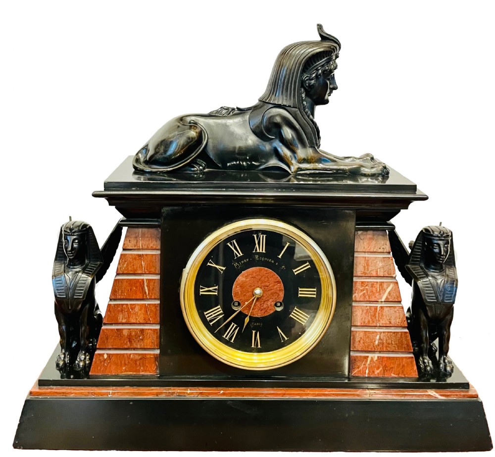An Egyptian Revival mantel clock constructed from black slate and red marble, topped with a reclining bronze sphinx and flanked by two seated sphinx figures.