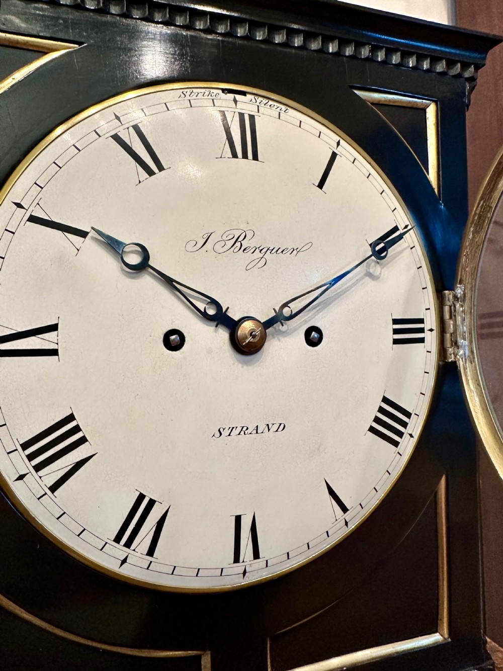 An antique Regency ebonised bracket clock with brass mounts, pineapple finial, ball feet, and a white dial signed J. Berguer Strand London. View IV
