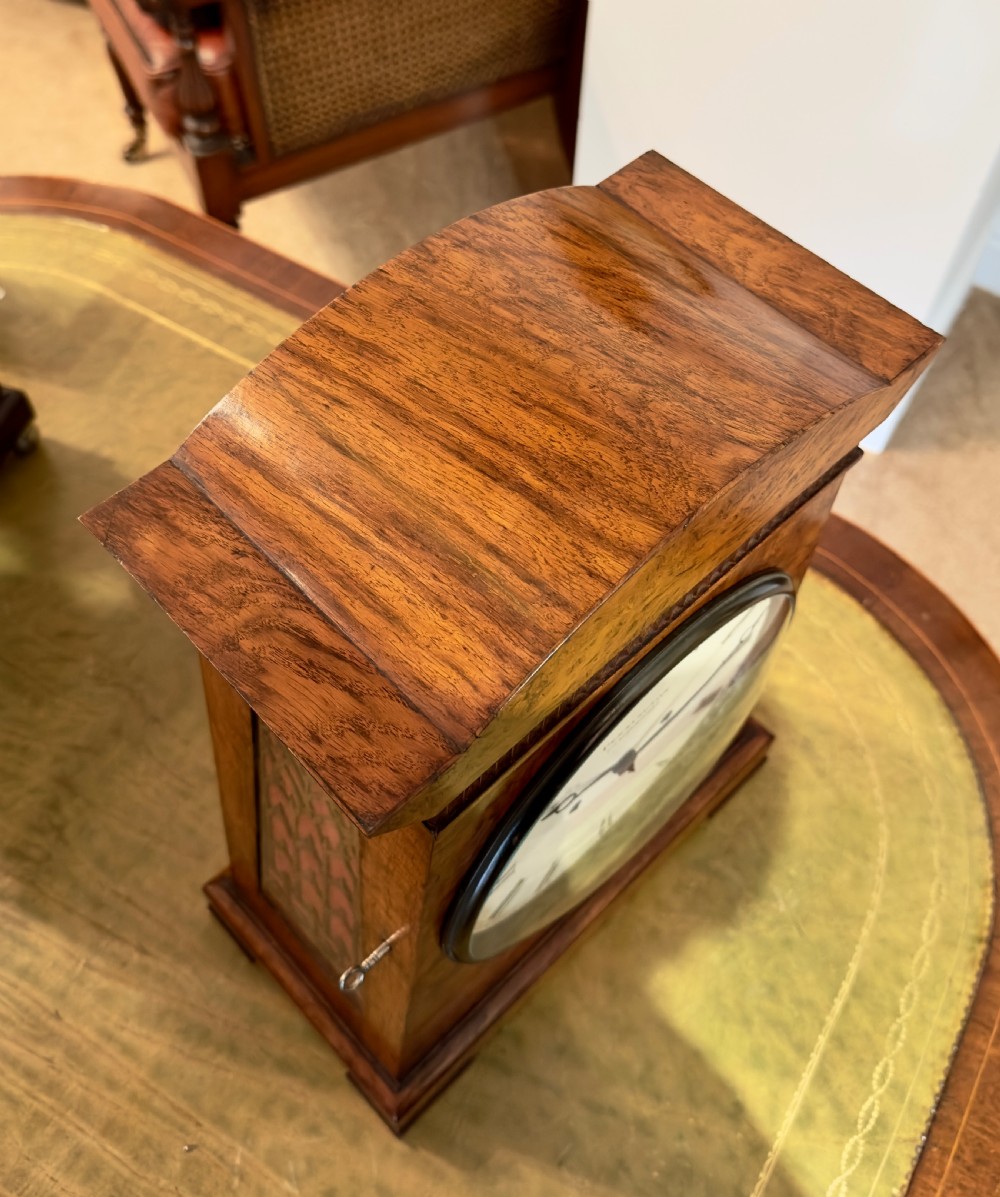 A rectangular pollard oak bracket clock featuring a shaped top, circular white dial with Roman numerals, and decorative side sound frets. View IV