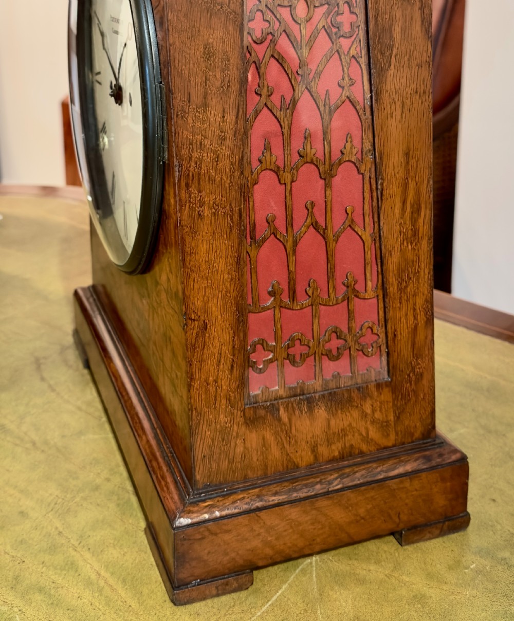 A rectangular pollard oak bracket clock featuring a shaped top, circular white dial with Roman numerals, and decorative side sound frets. View V
