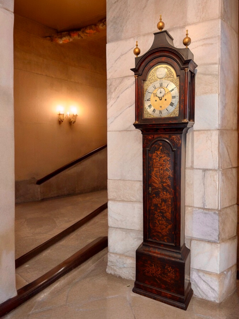 A tall antique Georgian Chinoiserie longcase clock with dark gilt lacquered oriental scenes, three brass finials, and a brass dial face.