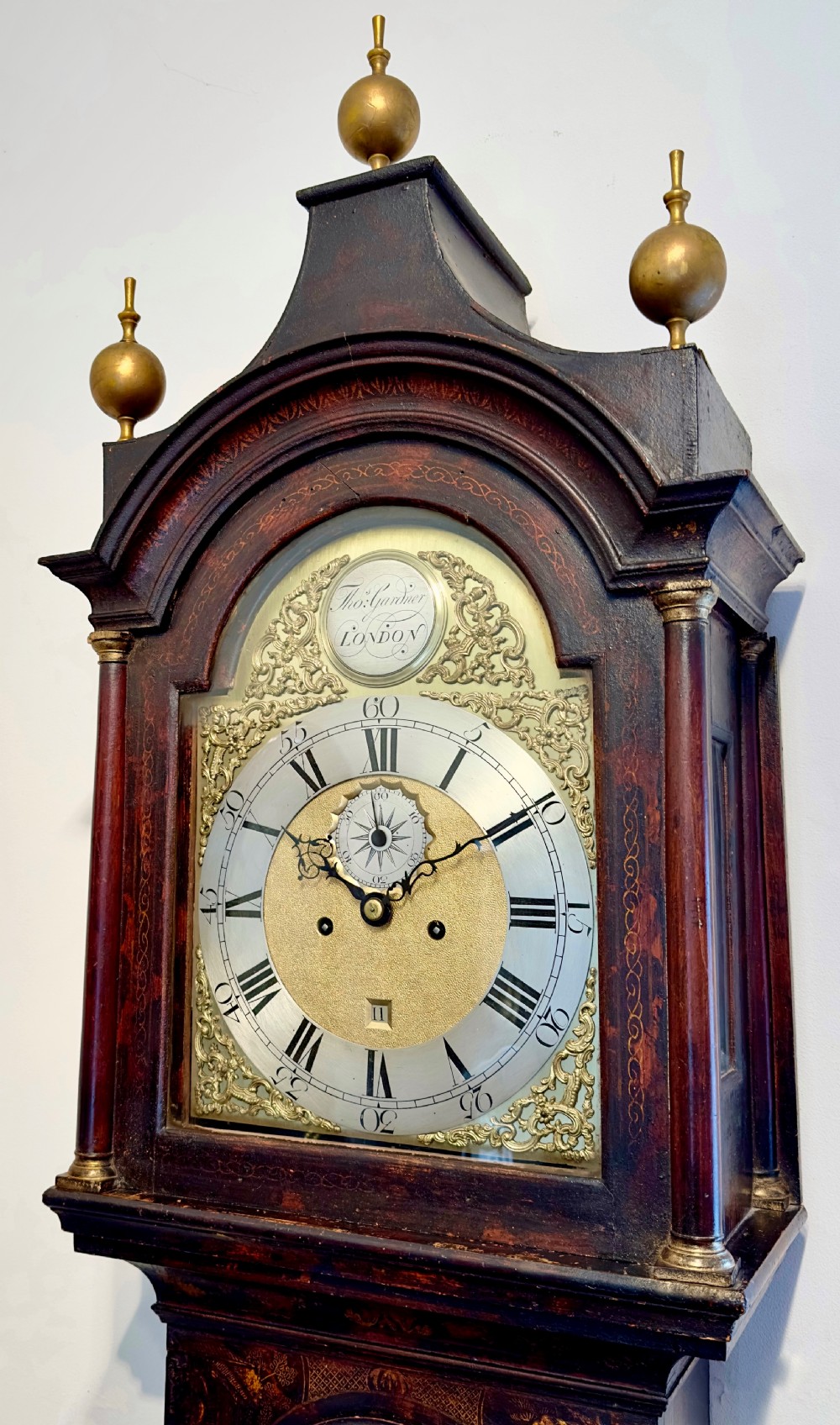 A tall antique Georgian Chinoiserie longcase clock with dark gilt lacquered oriental scenes, three brass finials, and a brass dial face. View II