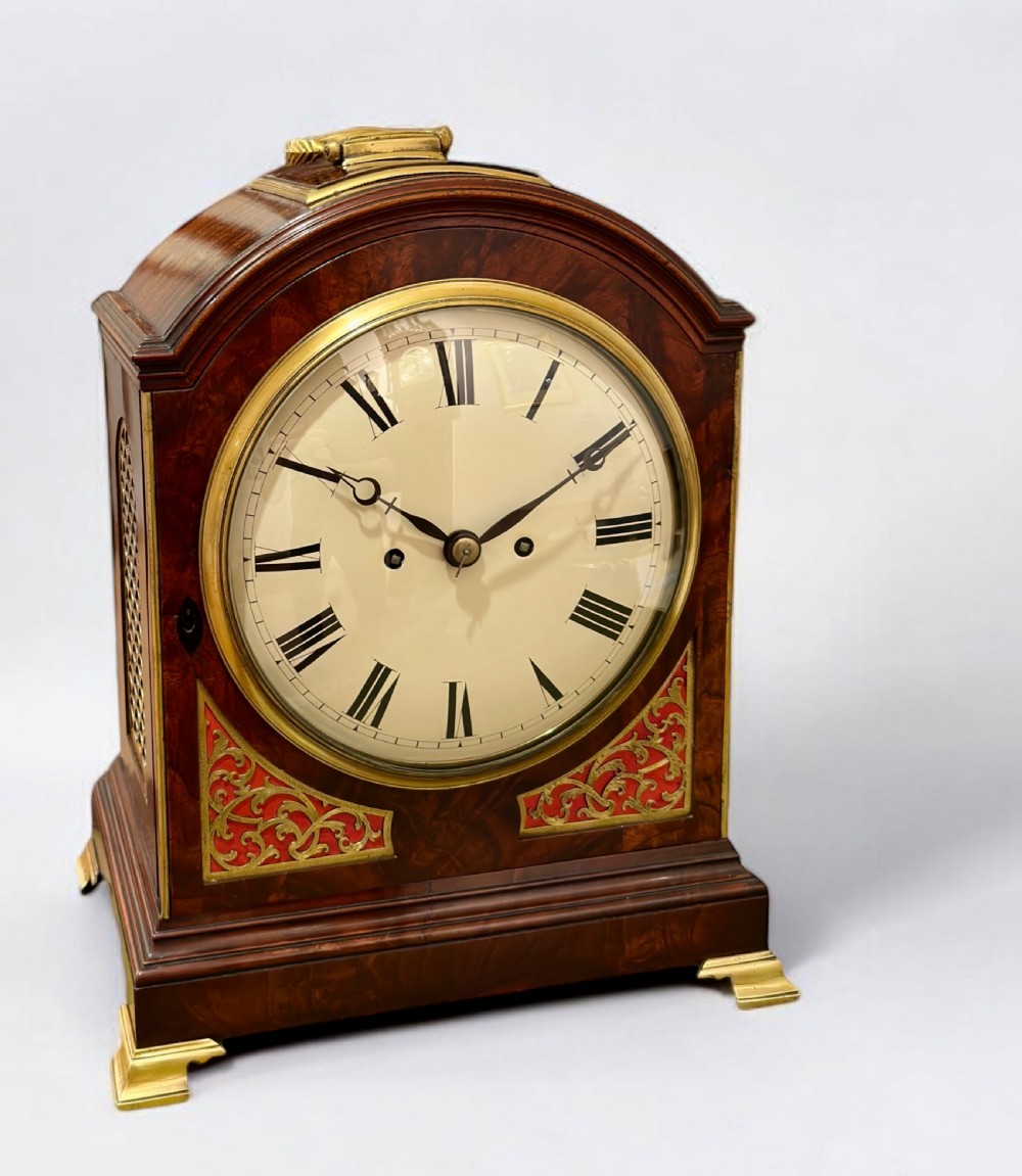 A Regency mahogany bracket clock featuring an arched case, brass carrying handle, circular dial with Roman numerals, and brass bracket feet.