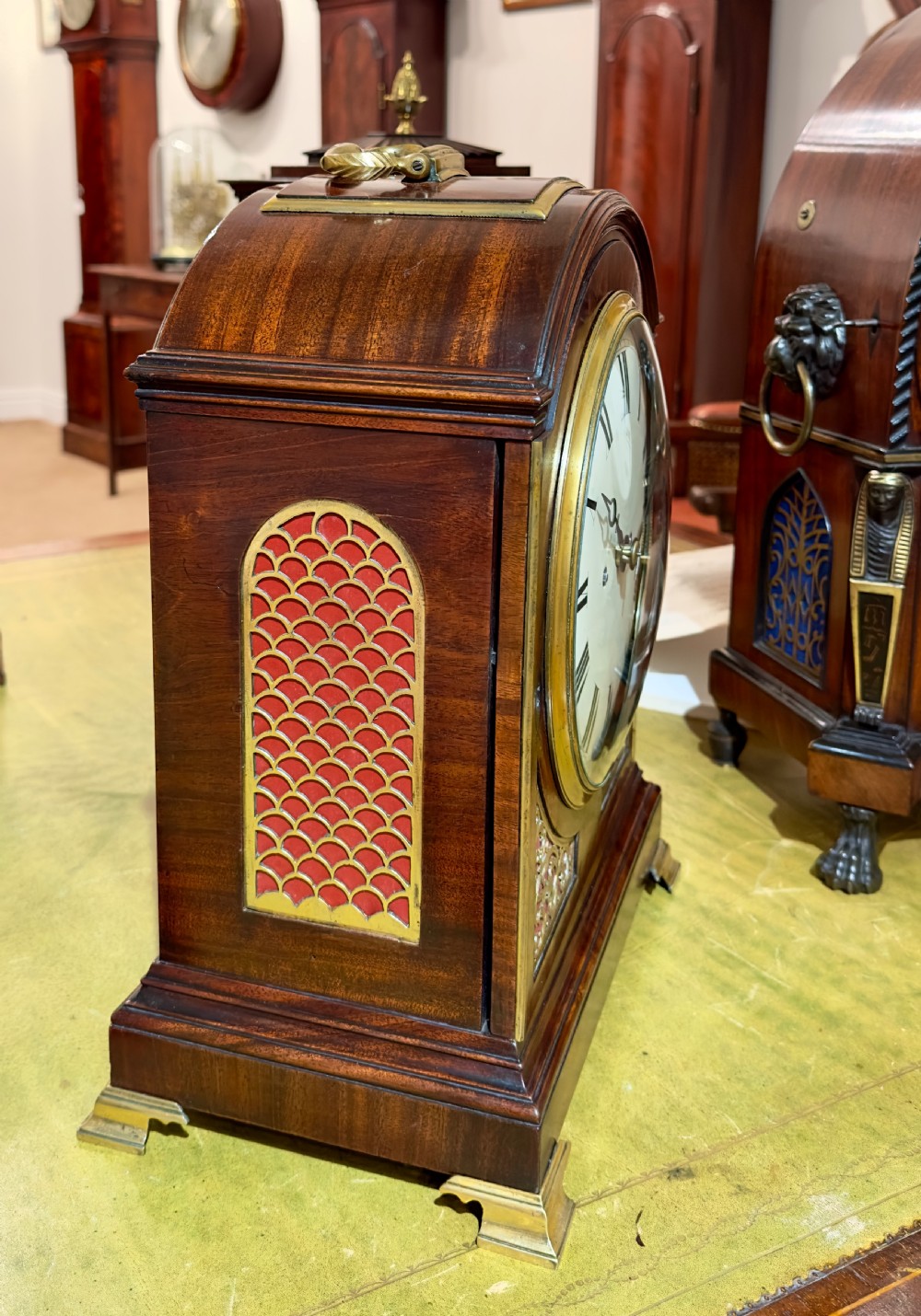 A Regency mahogany bracket clock featuring an arched case, brass carrying handle, circular dial with Roman numerals, and brass bracket feet. View II