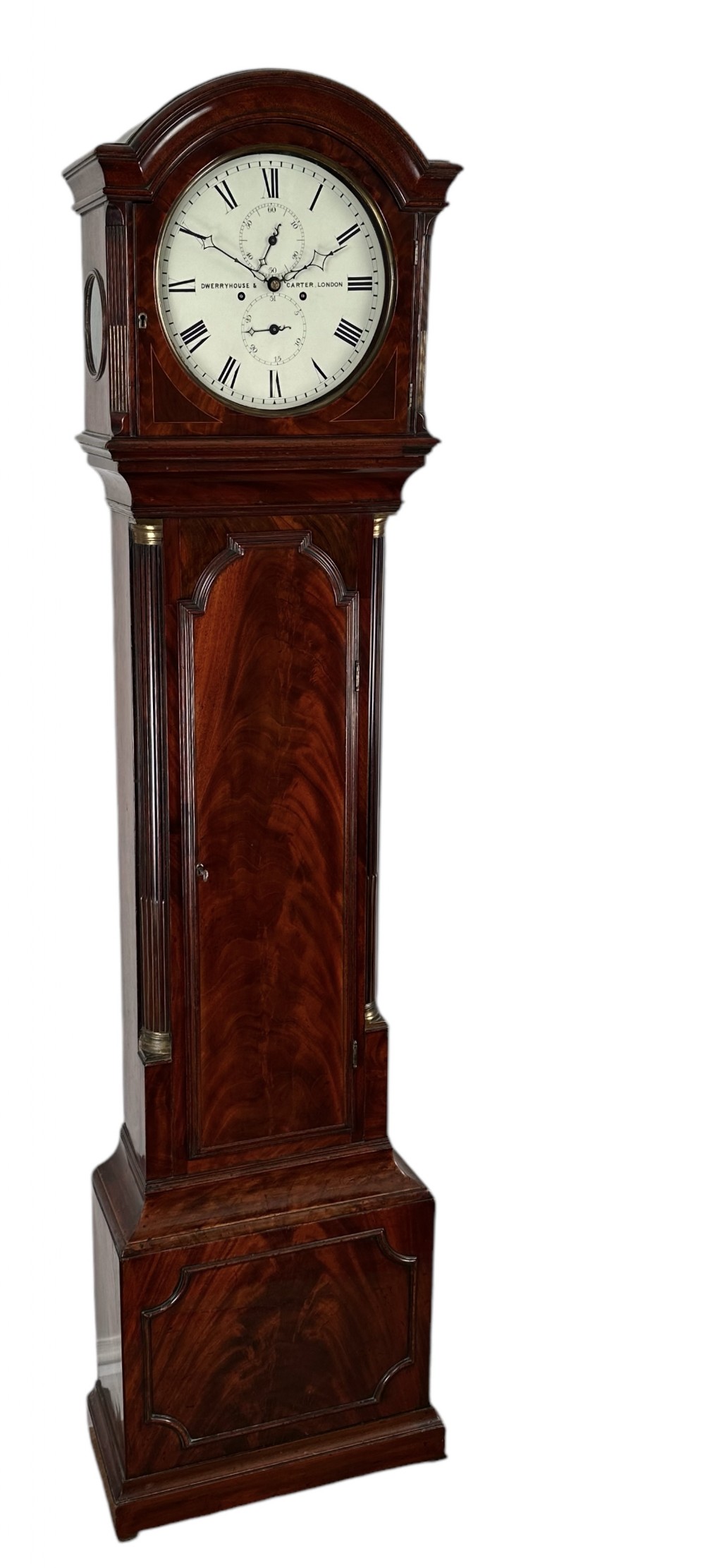 An antique mahogany longcase clock featuring an arched hood, a white circular dial inscribed Dwerrihouse and Carter London, and a flame mahogany trunk door with fluted columns.