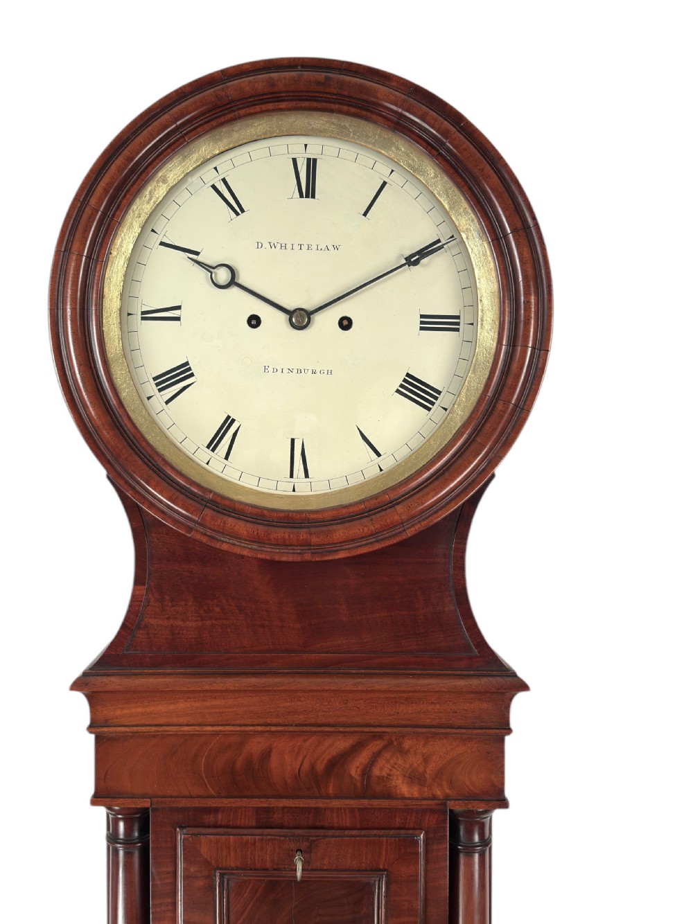 A Scottish Regency flame mahogany longcase clock featuring a circular brass-rimmed dial with Roman numerals and a veneered trunk on bracket feet. View III