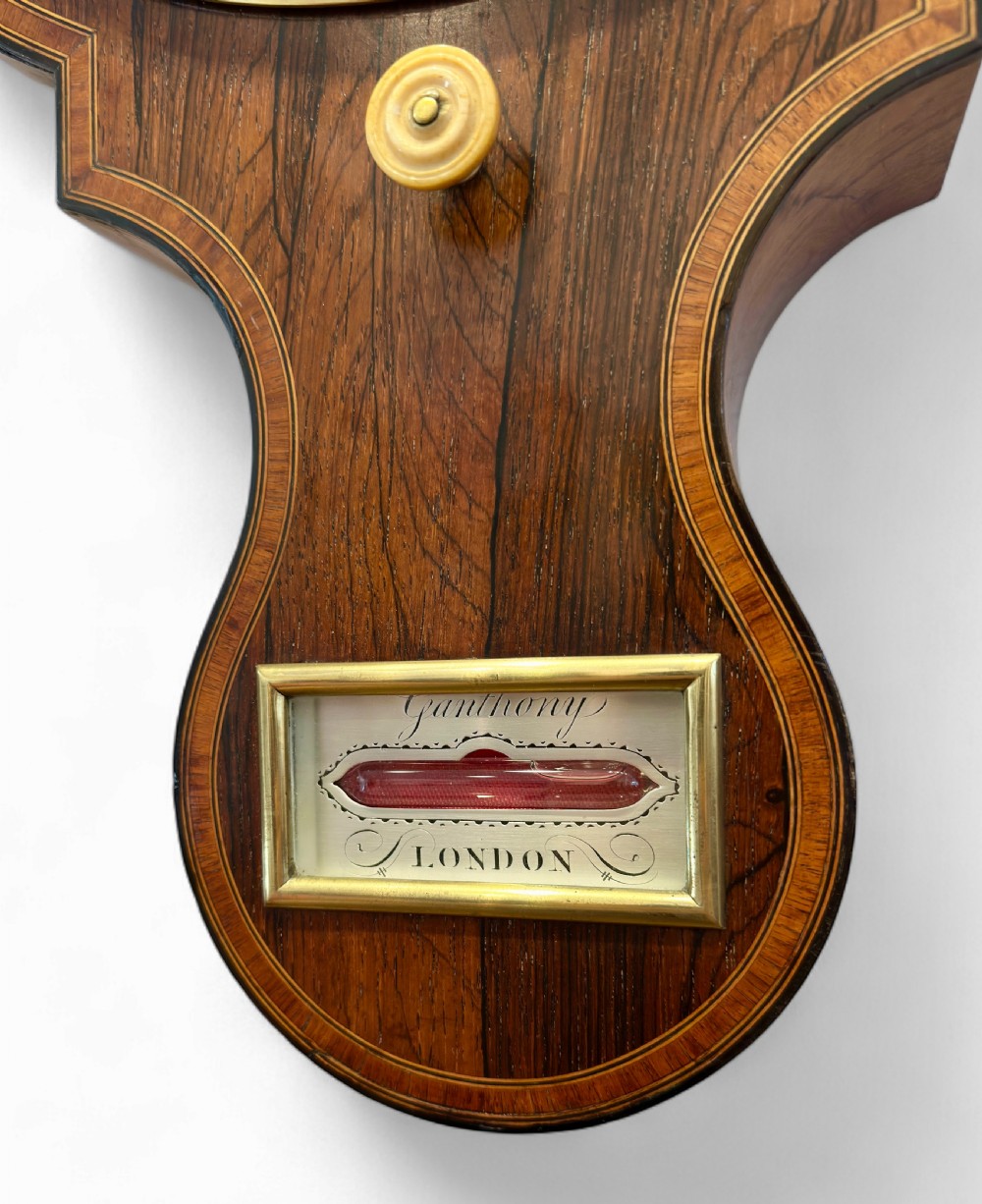 A vertical Regency rosewood banjo clock barometer featuring an inlaid wooden case, top hygrometer, thermometer tube, central clock dial, and large silvered barometer dial. View IV