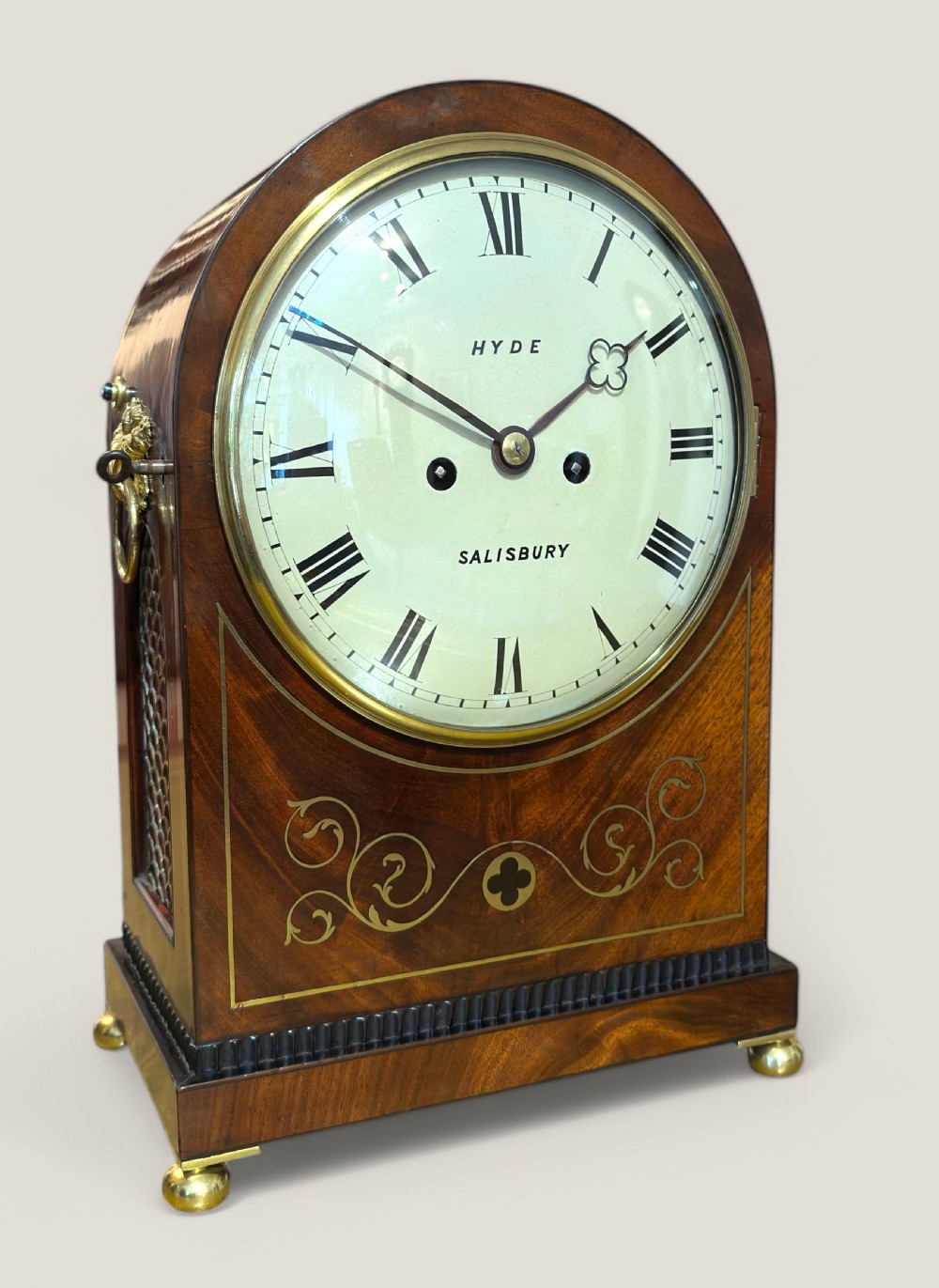 An arched antique mahogany bracket clock with brass scroll inlay, lion-mask ring handles, and a white dial signed Hyde Salisbury.