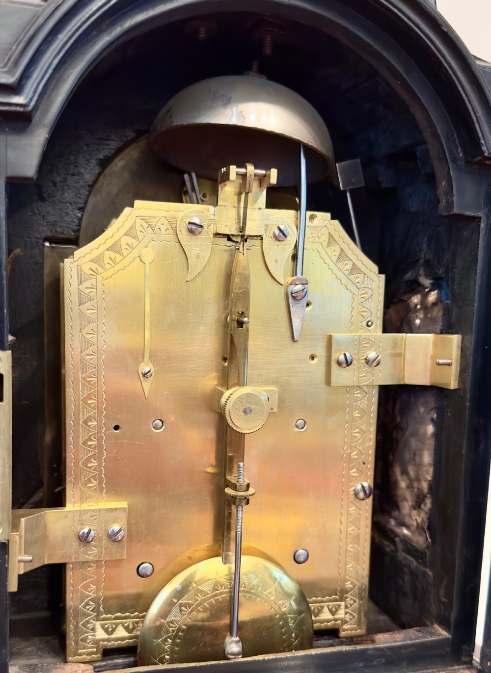 An English Regency ebonised bracket clock featuring an arched silvered dial, Roman numerals, a strike/silent selector, turned brass feet, and a brass carrying handle. View II
