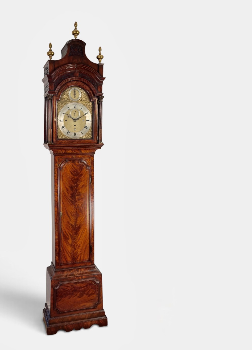 An eighteenth-century mahogany longcase clock featuring brass finials, an arched dial, and a figured flame mahogany trunk door.