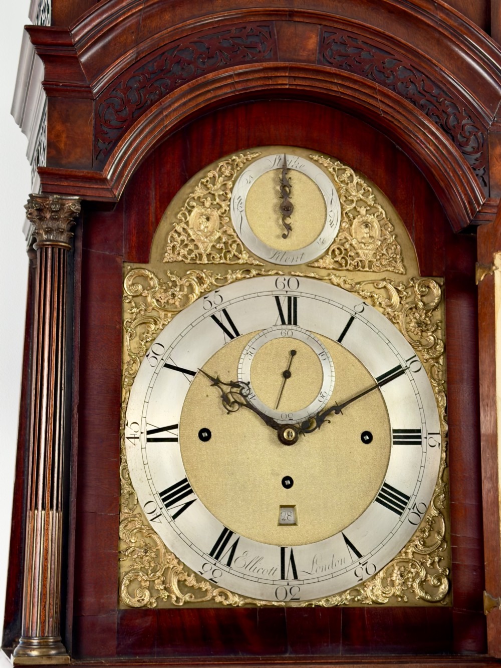 An eighteenth-century mahogany longcase clock featuring brass finials, an arched dial, and a figured flame mahogany trunk door. View IV