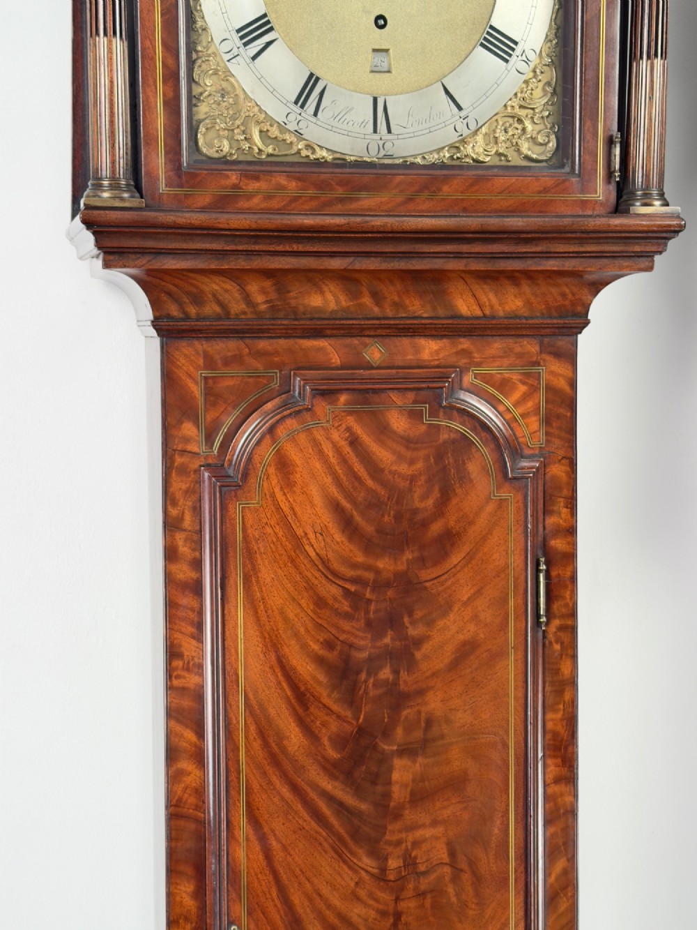 An eighteenth-century mahogany longcase clock featuring brass finials, an arched dial, and a figured flame mahogany trunk door. View V