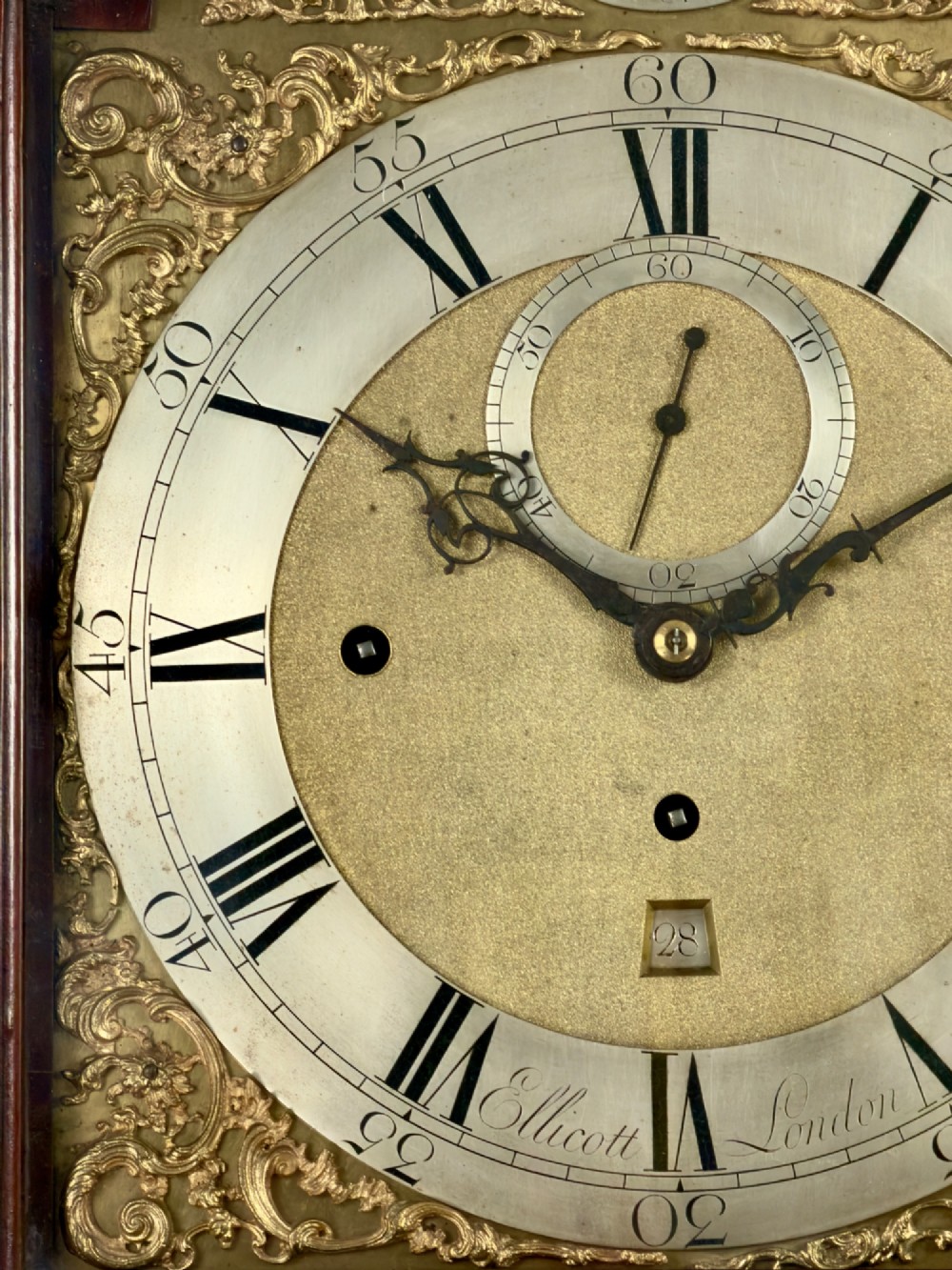 An eighteenth-century mahogany longcase clock featuring brass finials, an arched dial, and a figured flame mahogany trunk door. View VI
