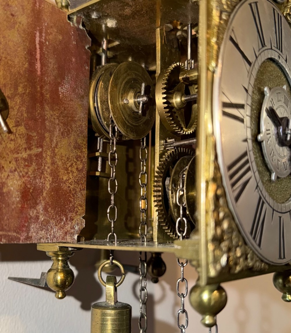 An antique miniature brass hook and spike wall clock with an engraved silvered chapter ring, ornate spandrels, and a top bell assembly. View III