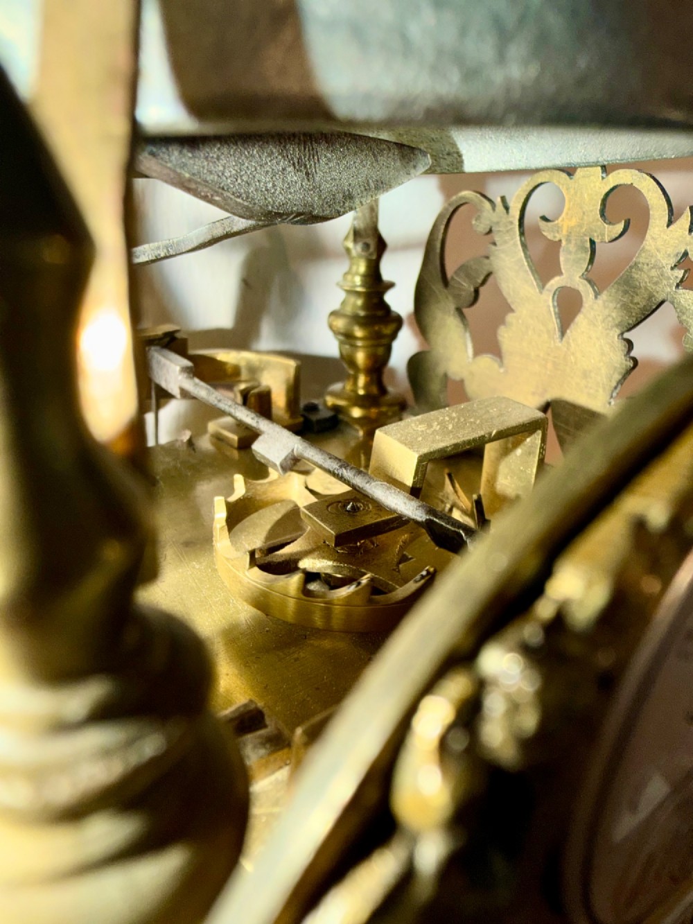 An antique miniature brass hook and spike wall clock with an engraved silvered chapter ring, ornate spandrels, and a top bell assembly. View IV