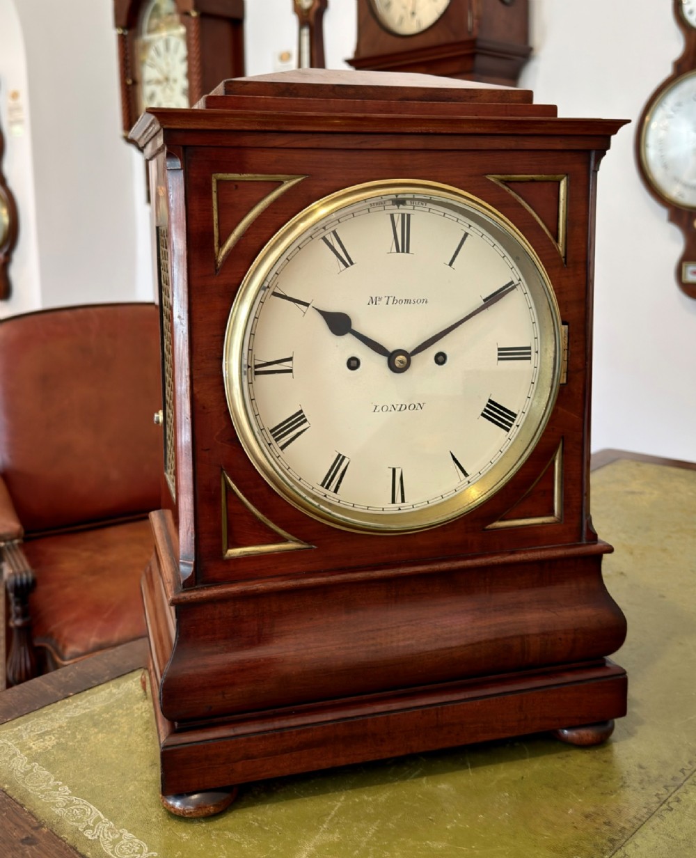 A Regency mahogany bracket clock featuring a cream dial with Roman numerals signed Thomson London, set within a brass-inlaid wooden case.