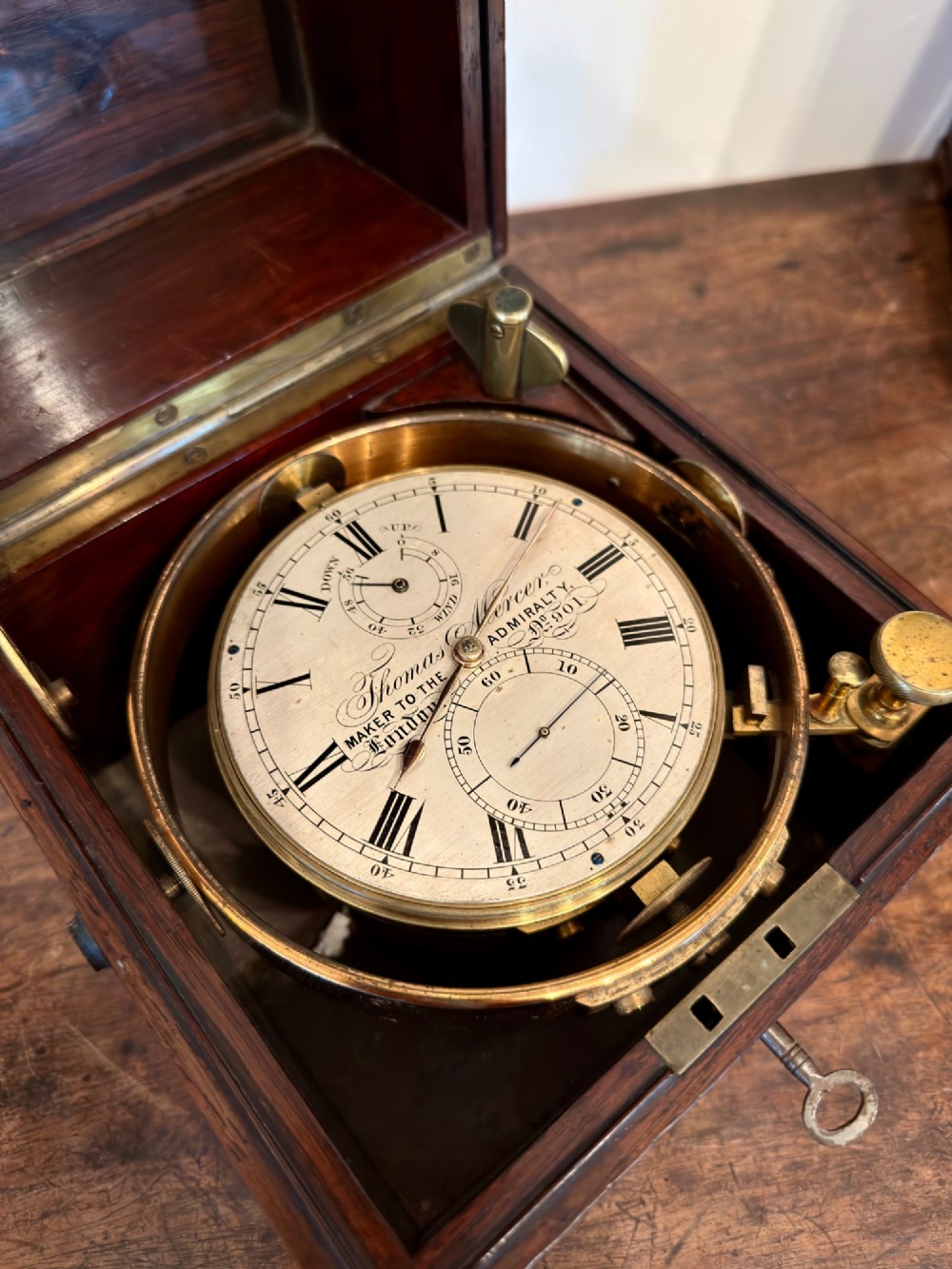 A Thomas Mercer marine chronometer with a silvered dial and brass gimbal mechanism set inside an open mahogany box.