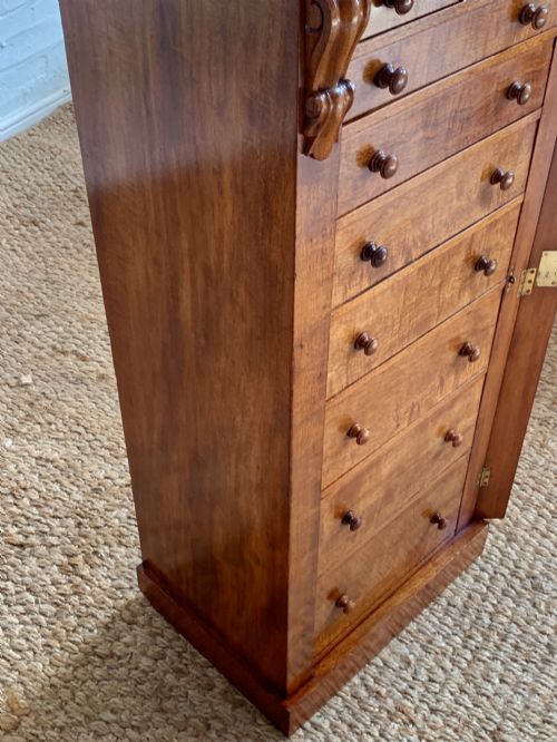 fig 4. A tall Victorian figured mahogany Wellington chest with eight graduated drawers, turned wooden knobs, carved corbels, and a hinged side locking bar.