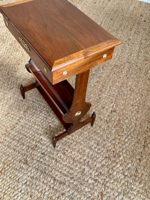 fig 3. A dark mahogany Canterbury side table featuring a rectangular top, a single shallow drawer with brass knobs, and a lower V-shaped magazine trough supported on shaped uprights.