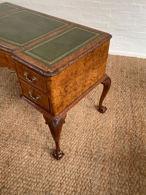 fig 1. A burr walnut kneehole writing desk with four drawers, carved cabriole legs with claw and ball feet, and a green leather writing surface.