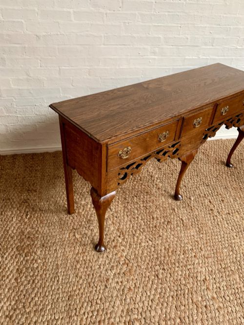 fig 1. An Edwardian oak dresser base featuring three drawers with brass handles, a decorative pierced fretwork apron, and four cabriole legs terminating in pad feet.