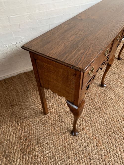fig 4. An Edwardian oak dresser base featuring three drawers with brass handles, a decorative pierced fretwork apron, and four cabriole legs terminating in pad feet.