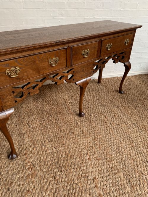 fig 5. An Edwardian oak dresser base featuring three drawers with brass handles, a decorative pierced fretwork apron, and four cabriole legs terminating in pad feet.