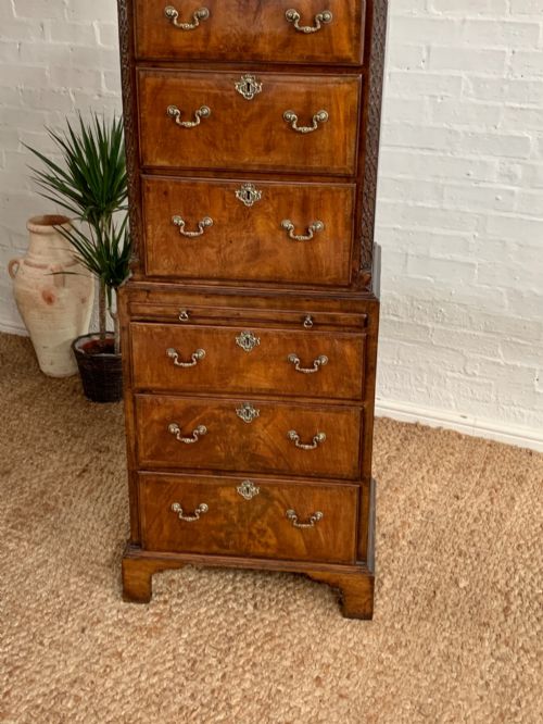 fig 3. A tall 19th-century George III style burr walnut chest of drawers featuring decorative brass handles, keyhole escutcheons, carved side friezes, and bracket feet.