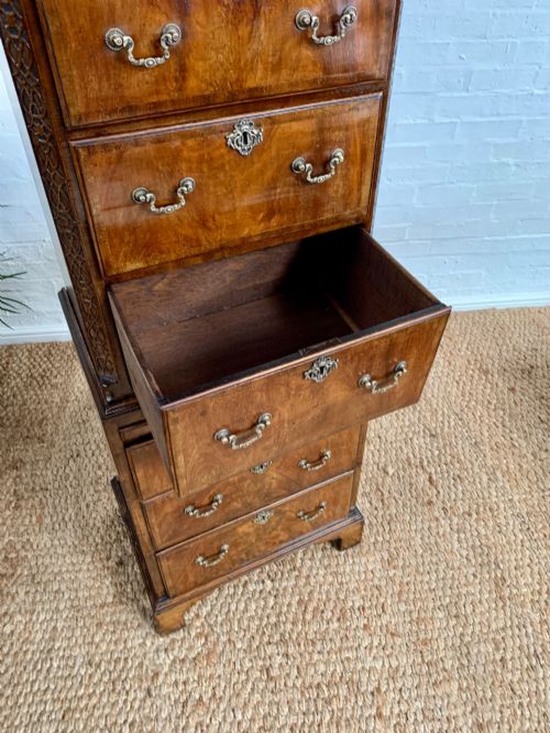 fig 4. A tall 19th-century George III style burr walnut chest of drawers featuring decorative brass handles, keyhole escutcheons, carved side friezes, and bracket feet.