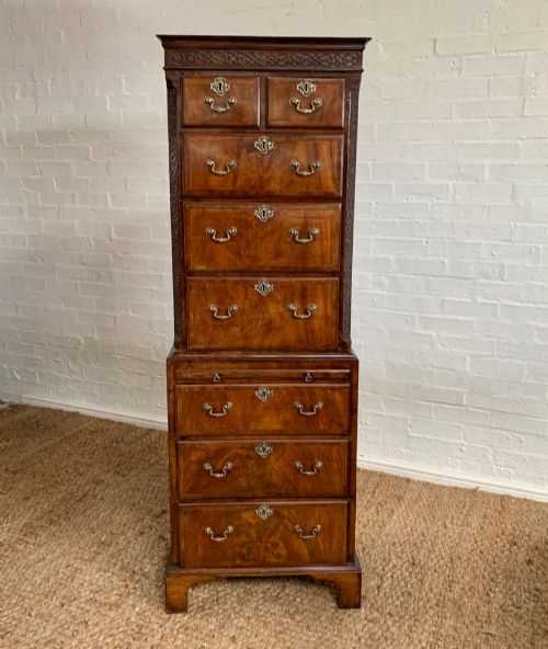 fig 2. A tall 19th-century George III style burr walnut chest of drawers featuring decorative brass handles, keyhole escutcheons, carved side friezes, and bracket feet.