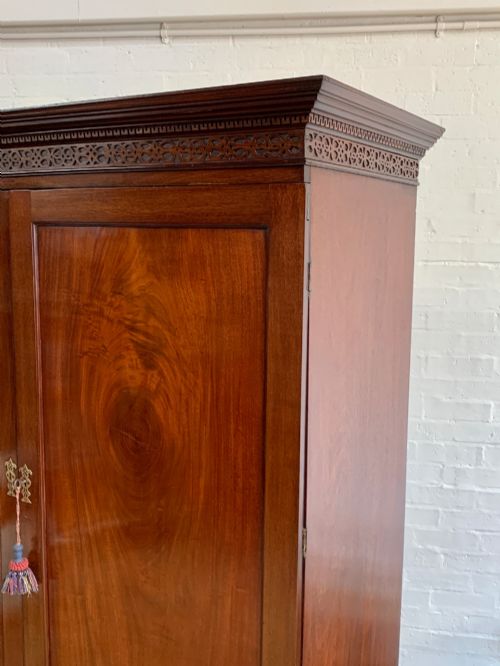 fig 1. A nineteenth-century dark mahogany linen press featuring a carved blind fretwork cornice, twin flame-mahogany cupboard doors, and four lower drawers with brass drop handles.
