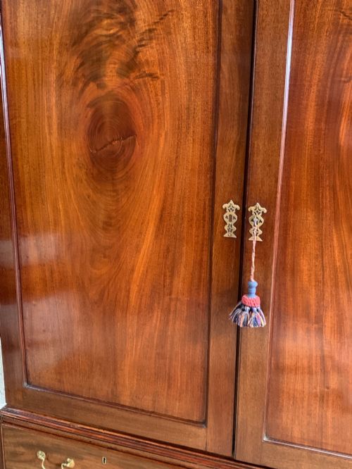 fig 2. A nineteenth-century dark mahogany linen press featuring a carved blind fretwork cornice, twin flame-mahogany cupboard doors, and four lower drawers with brass drop handles.