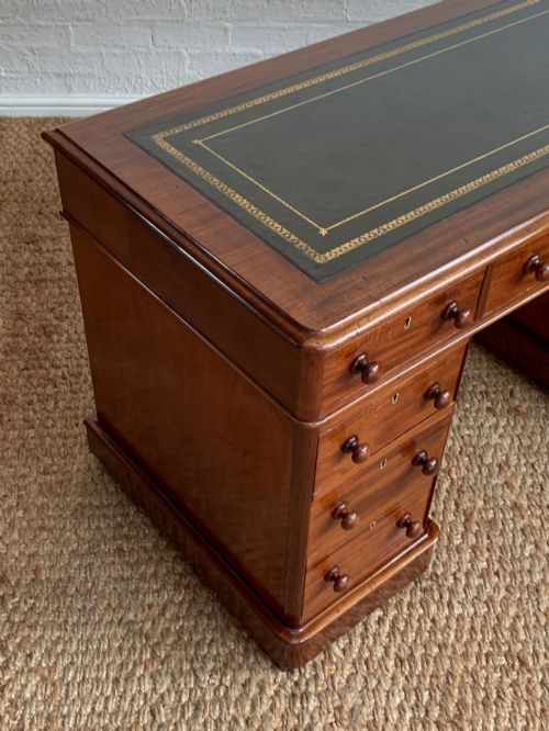 fig 1. Victorian mahogany pedestal desk featuring an olive green gold-tooled leather inset top and nine drawers with turned wooden knobs.