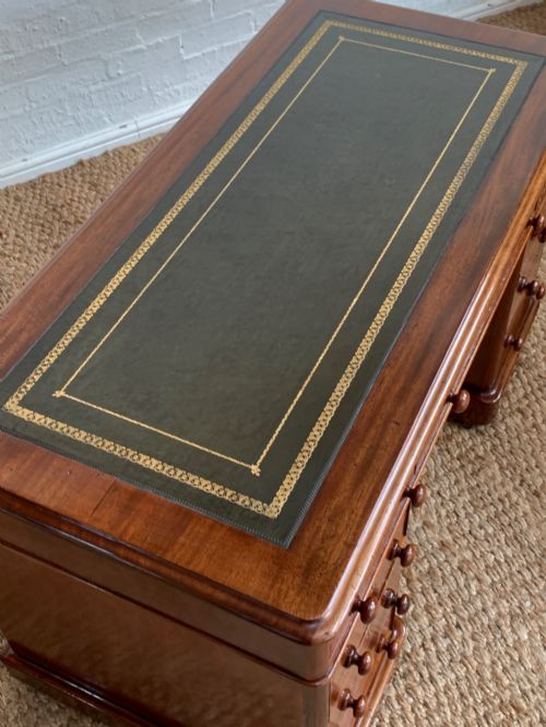 fig 2. Victorian mahogany pedestal desk featuring an olive green gold-tooled leather inset top and nine drawers with turned wooden knobs.