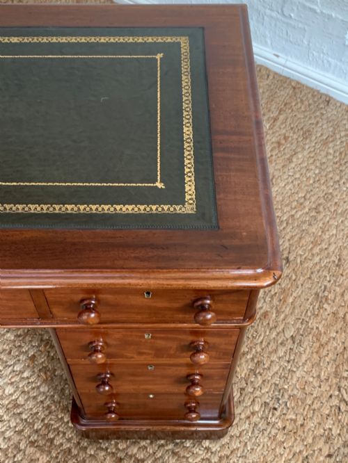 fig 3. Victorian mahogany pedestal desk featuring an olive green gold-tooled leather inset top and nine drawers with turned wooden knobs.