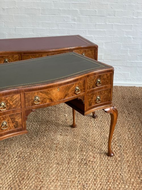 fig 1. An early 20th-century burr walnut writing desk featuring an inset leather top, kneehole drawer arrangement, brass drop handles, and cabriole legs.