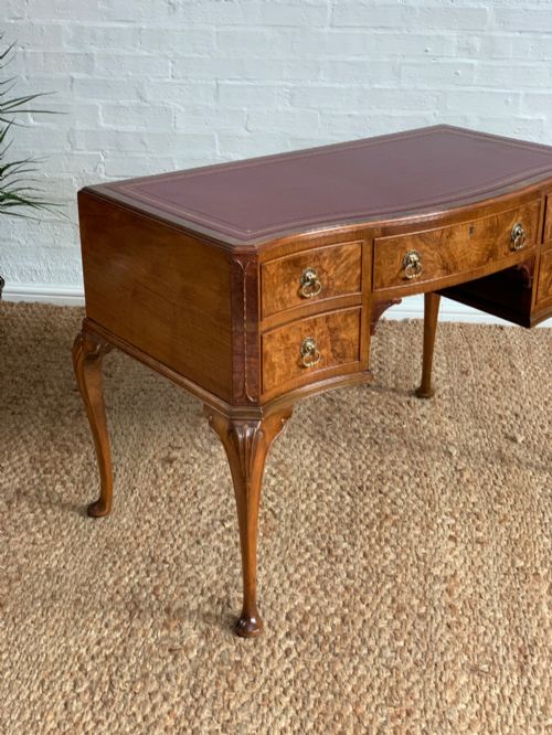 fig 1. An early 20th-century burr walnut writing desk featuring five drawers with brass handles, carved cabriole legs, and a fitted kneehole.