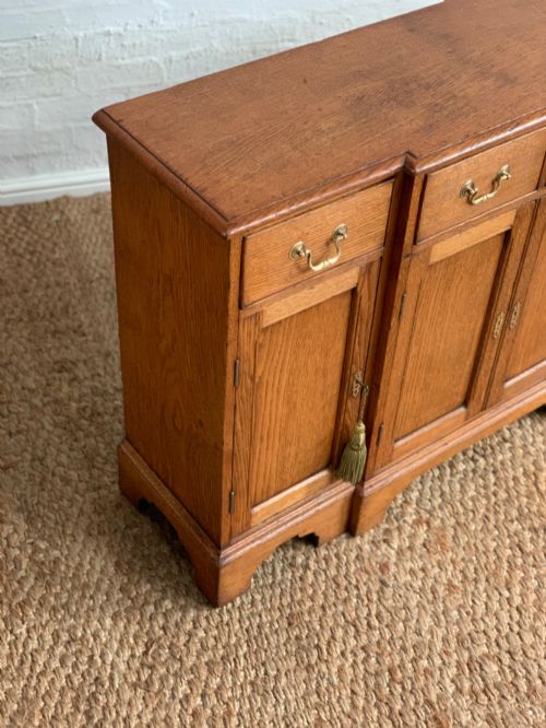 fig 3. A golden oak sideboard featuring four upper drawers, four panelled cupboard doors with brass handles, keyhole escutcheons with tassels, and bracket feet.