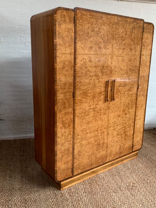 fig 1. An Art Deco double wardrobe crafted from figured burr walnut veneer with rounded top edges, vertical wooden handles, and a stepped plinth base.