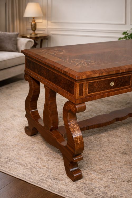 fig 1. A rectangular walnut writing desk featuring decorative corner marquetry, three frieze drawers with brass pulls, curved lyre-shaped legs, and a shaped central stretcher.