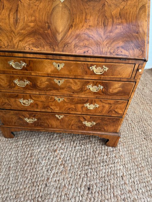 fig 5. A Georgian period figured walnut bureau featuring a slant front flap above four graduated drawers with brass handles, resting on bracket feet.