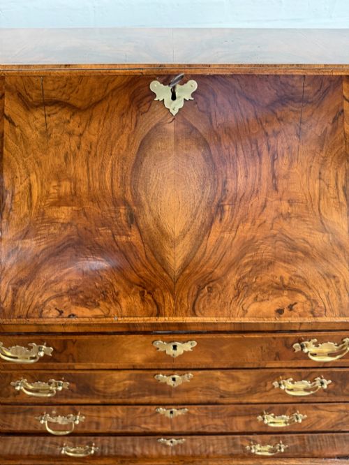 fig 6. A Georgian period figured walnut bureau featuring a slant front flap above four graduated drawers with brass handles, resting on bracket feet.
