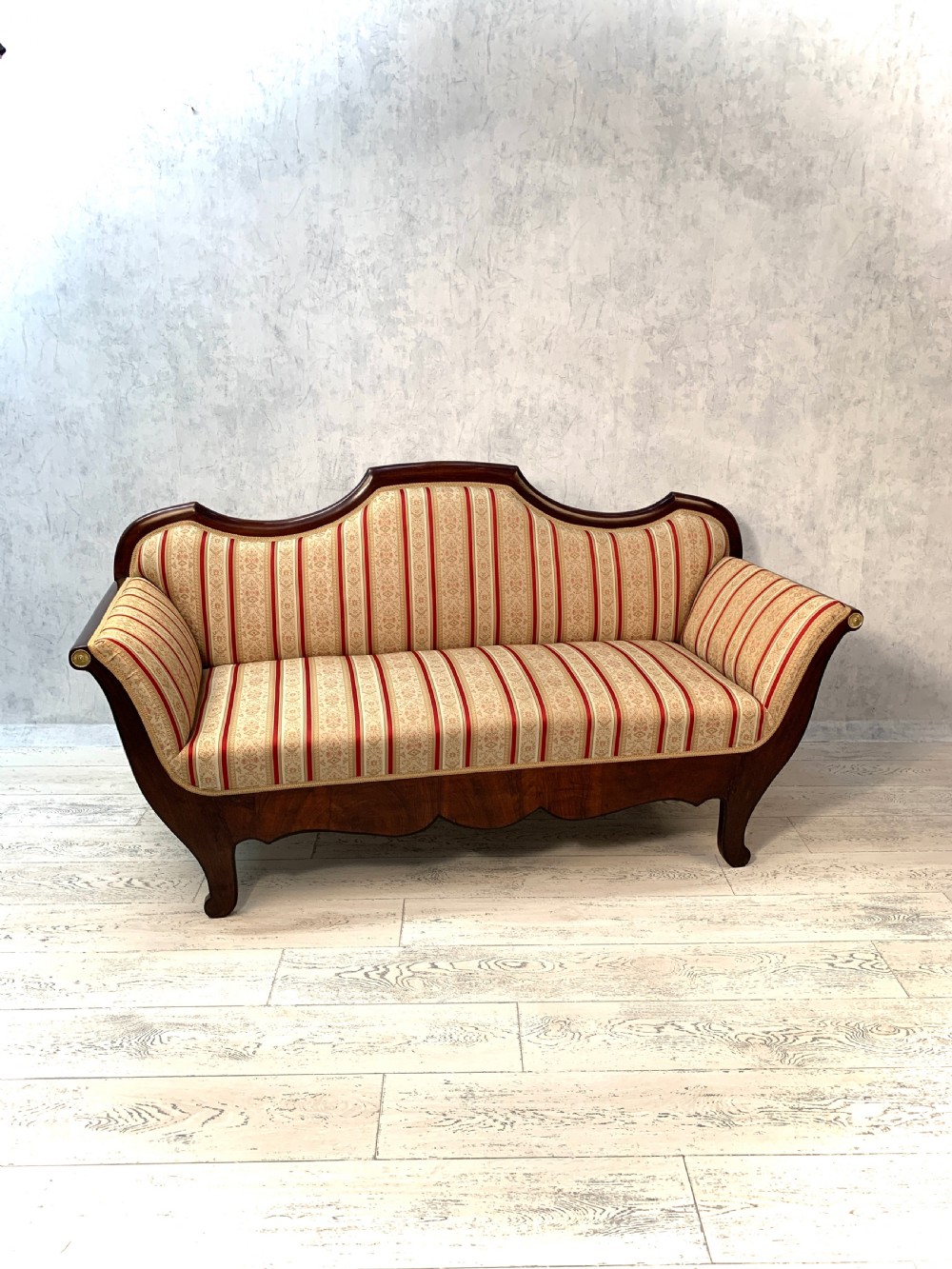 An antique Biedermeier three-seater sofa featuring a polished dark wood frame with sweeping scroll arms and red and cream striped upholstery.