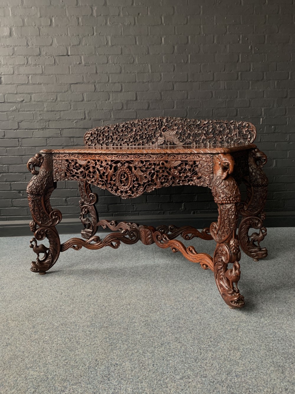 An intricately hand-carved 19th-century Anglo-Indian rosewood console table featuring a pierced floral back gallery, carved apron, and ornate bird-form legs.