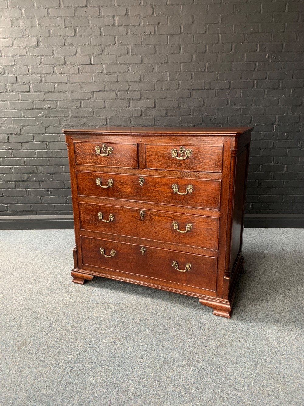 A George III solid oak chest of drawers featuring a two-short-over-three-long drawer configuration, brass swan-neck handles, keyhole escutcheons, and bracket feet.